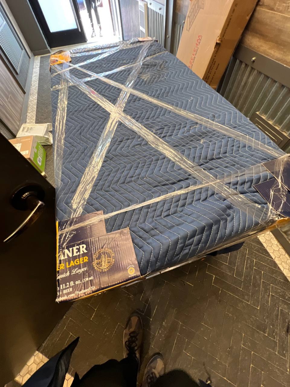Large furniture piece wrapped in a moving blanket and reinforced at corners